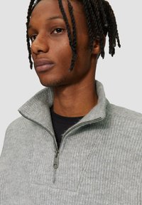 Grau zip-versehener Pullover aus strukturiertem Stoff, mit hohem Kragen und einem Reißverschluss mit metallischem Akzent. Eine Nahaufnahme zeigt den Ausschnitt.