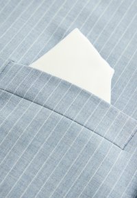 Heledu sinine triibuline kangas, millel on kotis selgelt nähtav valge linane salvrätik, rõhutades sileda tekstuuri ja kohandatud disaini.