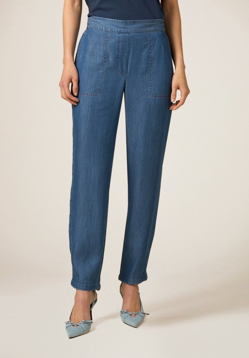 Femme portant un pantalon en jean bleu à jambes droites avec des poches plaquées à l'avant et des ourlets retroussés, associé à des talons pointus bleu clair.