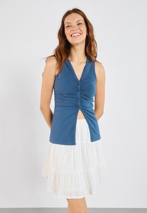 Blue sleeveless top with a V-neck, button detailing, and gathered texture, paired with a white tiered skirt. Simple and classic design.