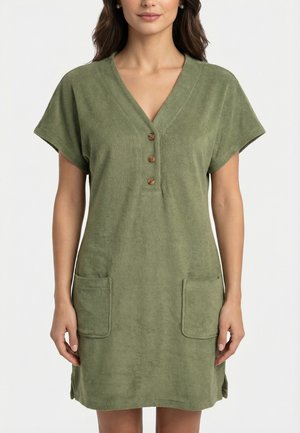 Femme portant une robe olive verte, courte, à manches courtes, avec trois boutons sur le devant et deux poches plaquées.