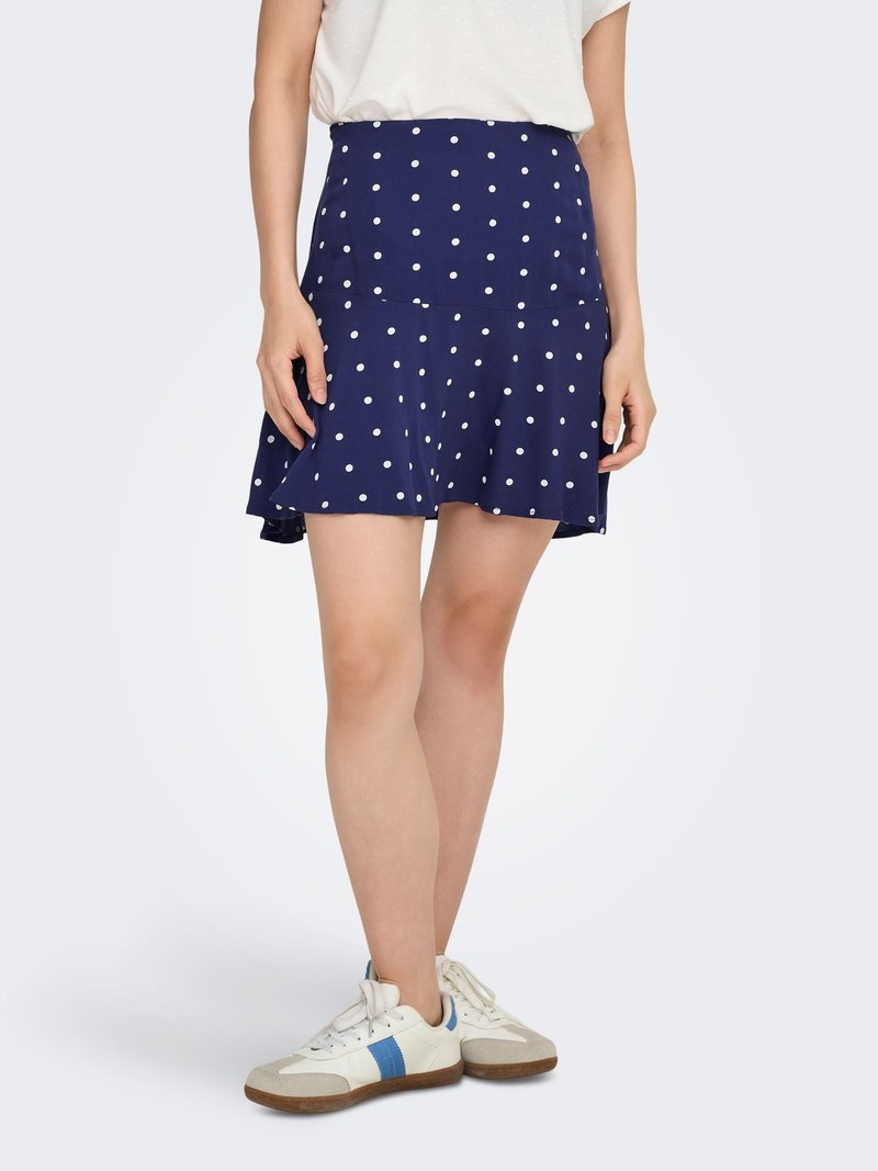 Gonna a pieghe blu navy con pois bianchi e una vita alta. Indossata con sneakers bianche con dettagli blu e suola texturizzata.