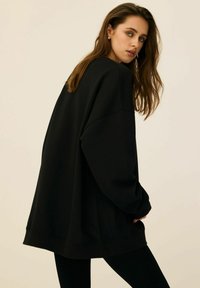 Czarny, oversized sweatshirt z długimi rękawami i luźnym krojem, z ryflowanym wykończeniem dołu i mankietów. Gładka tekstura tkaniny, minimalistyczny design.