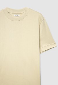 T-shirt beige clair à manches courtes avec un col rond, en tissu doux, présentant une texture subtile et des manches retroussées pour une coupe décontractée.