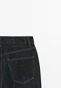 Jeans in denim scuro con vita alta, caratterizzati da una tasca posteriore singola con cucitura a contrasto e una finitura pulita e minimalista.