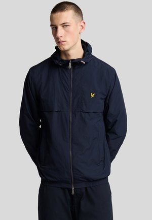 Marinblå lätt jacka, texturerad tyg, framdragkedja, huva, två stora bröstfickor, gul logotypaccent på vänster bröst.