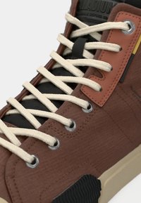 Καφέ πάνινο αθλητικό παπούτσι με εκρού κορδόνια, μαύρες λεπτομέρειες και υφή στην επιφάνεια. Διαθέτει λαστιχένια σόλα και αντιθετικές χρωματικές λεπτομέρειες.