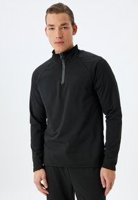 Sudadera atlética negra con cuello y media cremallera en la parte delantera. Confeccionada con una tela suave y elástica, presenta mangas raglán y un ajuste ceñido.