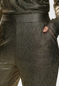 Pantaloni aurii metalici cu un model negru, având o suprafață texturată și un luciu subtil, cu un buzunar lateral și un talie ajustată.