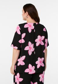 Krótki rękaw bluzka w kolorze czarnym z dużym różowym wzorem kwiatowym. Posiada okrągły dekolt oraz subtelne zapięcie z tyłu. Gładka tekstura materiału.