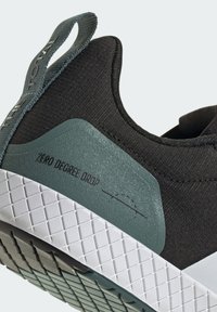 Black athletic shoe with a textured black fabric upper, green accent, and a white, patterned sole. Features a heel tab labeled "ZERO DEGREE DROP."