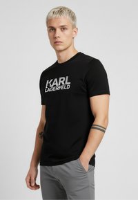 Czarny t-shirt z krótkim rękawem z białym logo „KARL LAGERFELD”. Wykonany z gładkiej tkaniny, z okrągłym dekoltem i dopasowanym krojem.