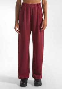 Bordeaux wijde broek van zachte stof, met geplooide voorkant en elastische tailleband, gecombineerd met zwarte sneakers.