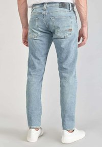 Vaqueros de color azul claro con corte recto, textura desvaída, dos bolsillos traseros y una etiqueta de cuero en la cinturilla, combinados con zapatillas blancas.