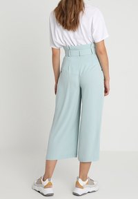 Light blue, high-waisted culottes with a wide leg and back belt detail, paired with white and gray sneakers, viewed from the back.