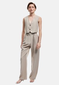 Beige cropped vest med to knapper, parret med højtaljede beige bukser med plissee og bindebælte. Glat stofstruktur.
