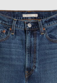 Dark blue denim jeans with a high waist, front button closure, and copper stitching. Features two front pockets and a brand tag inside.