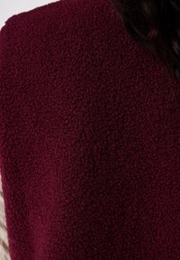 Tissu polaire bordeaux avec une surface douce et texturée ; le matériau semble épais et confortable, présentant un design simple sans éléments métalliques visibles.