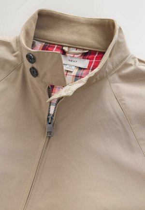 Beige jacket made of lightweight material with a zippered front, brown ribbed collar, and red plaid lining. Features two black button accents.