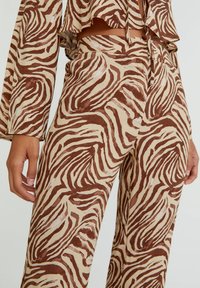 Pantalons taille haute et haut assorti avec des rayures zèbre marron et crème, portés par une personne avec des mains et un ventre visibles.