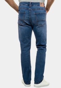 Denim jeans in dark blue, straight cut with a slightly faded texture. Features two back pockets, stitching accents, and a branded tag on the waistband.