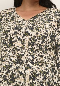 Bluse med blomstermønster i creme, sort og olivengrøn. Har en V-hals og let stof med en blød tekstur.