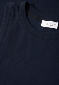 Top senza maniche di colore blu navy realizzato in tessuto morbido, con scollatura rotonda e un'etichetta con la scritta "STREET ONE STUDIO" sulla cucitura interna.
