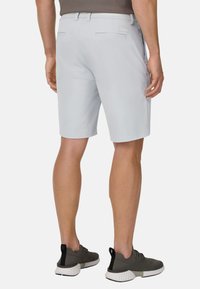 Hellgraue Shorts mit glatter Textur, flacher Vorderseite, zwei Gesäßtaschen und tailliertem Bund. Kombiniert mit grauen Sportschuhen mit weißen Sohlen.