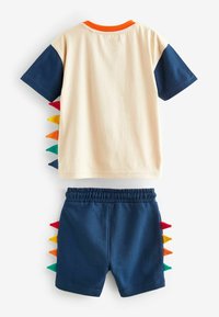 Short-sleeve T-shirt in cream with dark blue sleeves and an orange collar, paired with navy shorts featuring multicolor spikes on sides.