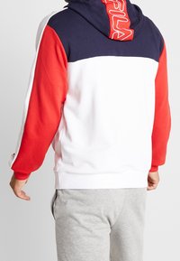 Sudadera con bloques de color en rojo, azul marino y blanco. Fabricada en tela suave con bolsillos tipo canguro y puños acanalados. Presenta el logo en la capucha.