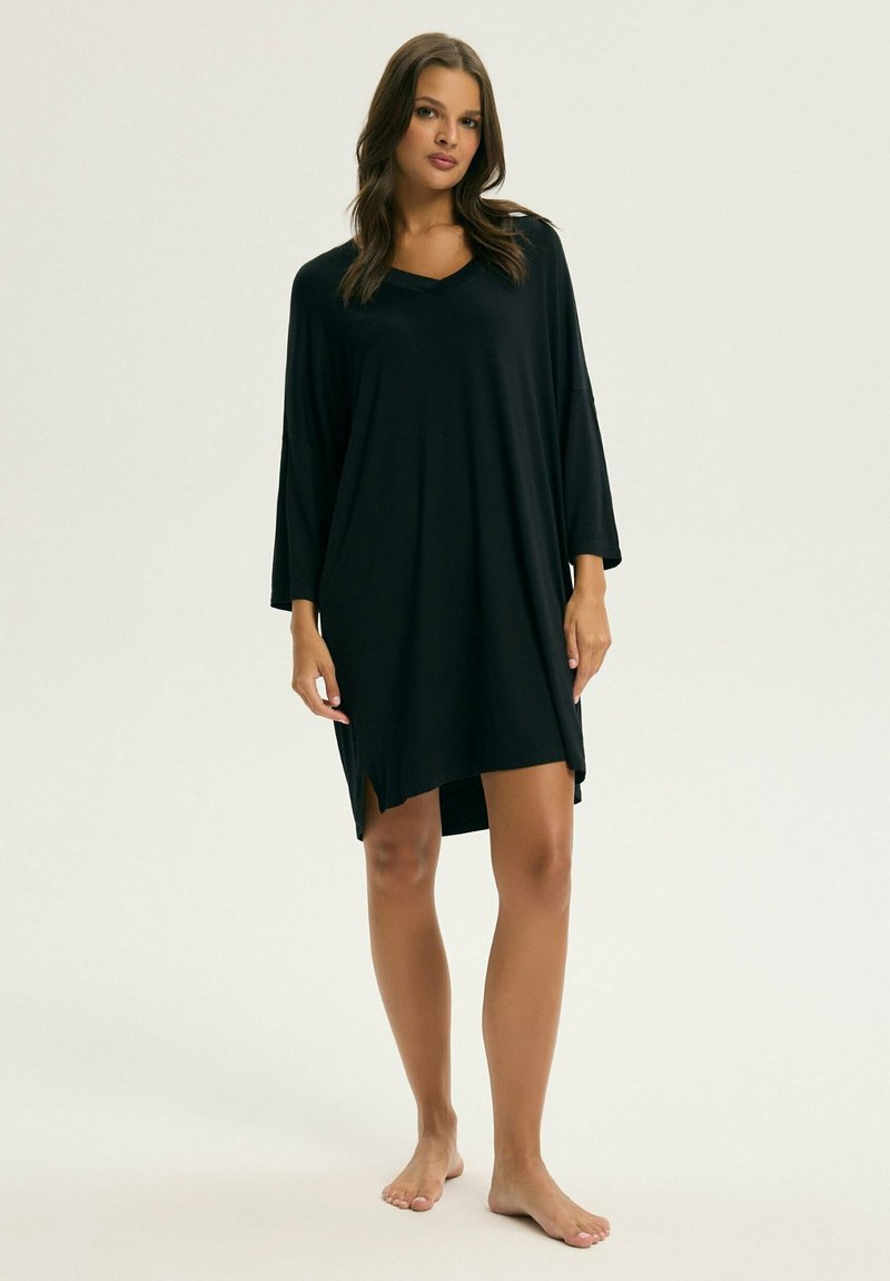 Czarna, oversize sukienka z dekoltem w kształcie litery V, rękawami 3/4, bocznymi rozcięciami oraz miękką, gładką fakturą. Sukienka sięga nad kolano.