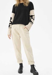 Pull noir et beige en tricot avec des manches à motifs, associé à un pantalon crème retroussé aux chevilles et des bottes noires à lacets.