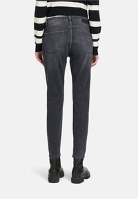 Jean gris foncé avec une coupe slim, un design à cinq poches et des coutures subtiles. Porté avec un haut à rayures noir et blanc à manches longues et des bottes noires.