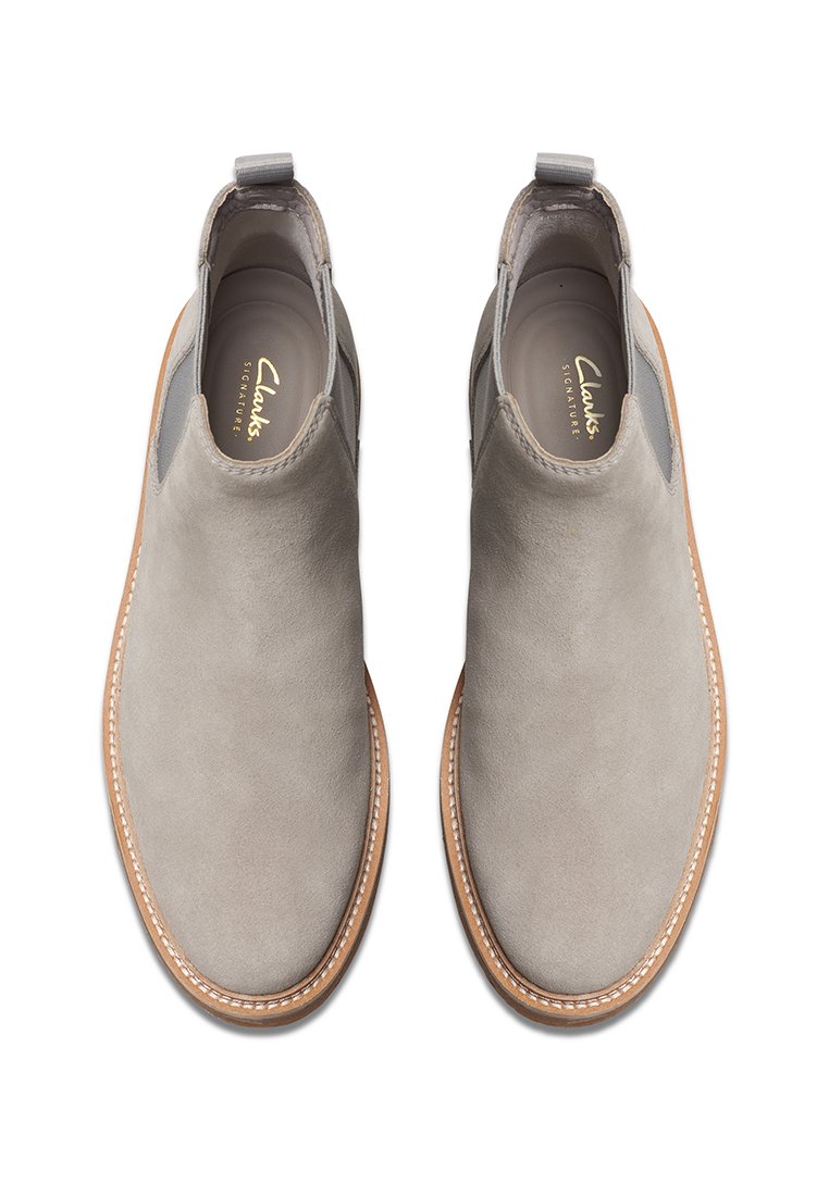 Graue Wildleder-Stiefeletten mit elastischen Seitenpaneelen und einer braunen Gummisohle, die eine gestickte Kante und ein prägtes Logo im Inneren aufweisen.
