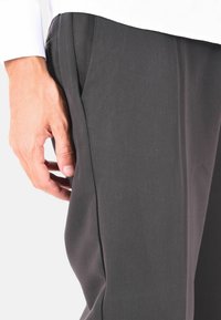 Pantaloni grigi realizzati in tessuto testurizzato, caratterizzati da un design elegante e tasche laterali, con una mano posizionata vicino alla vita.