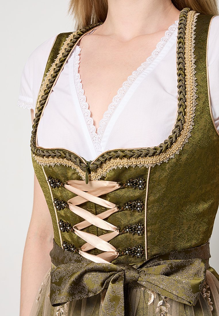 Dirndl-Kleid aus olivgrünem Seide mit Spitzenbesatz, dekorativer Schnürung und perlenartigen Akzenten. Schleife in der Taille, kombiniert mit einer weißen Bluse darunter.
