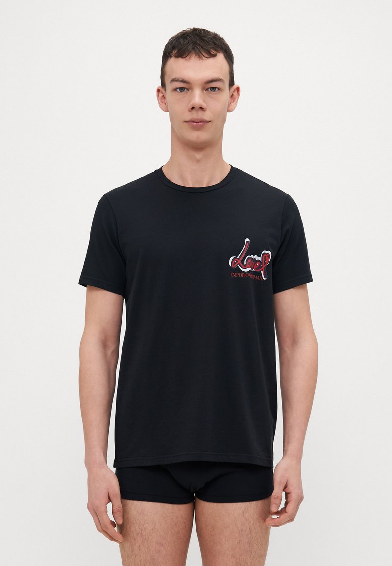T-shirt nera a maniche corte con collo rotondo, caratterizzata da una grafica colorata e testo "love" sulla parte sinistra del petto. Materiale in cotone morbido.