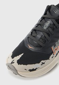 Μαύρο αθλητικό παπούτσι με υφασμένο συνθετικό επάνω μέρος, γκρι λεπτομέρειες και αφηρημένο λευκό σχέδιο. Διαθέτει έντονο σύστημα κορδονιών και λογότυπο της μάρκας.