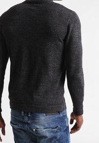 Dark grey, textured sweater with a ribbed collar, long sleeves, and a snug fit, paired with blue denim jeans featuring pockets.