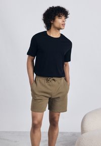 Tricou negru cu mânecă scurtă, asortat cu pantaloni scurți texturat bej, având talie elastică și șnur, expus pe un fundal neutru.