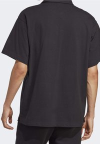 Černé polo tričko vyrobené z bavlny, se klasickým límečkem, krátkými rukávy a volným střihem. Jednoduchý design bez viditelných vzorů.