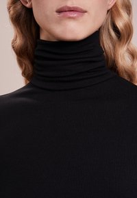 Schwarzer, gerippter Rollkragenpullover mit figurbetontem Design. Der Stoff ist strukturiert mit vertikalen Rillen und verfügt über einen hohen, umgeschlagenen Kragen.