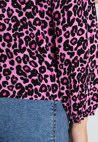 Kortärmad blus med ett rosa tyg och djärvt svart leopardmönster, samlade muddar och avslappnad passform vid fållen, kombinerad med denim.