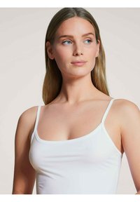 White camisole with thin straps, features a fitted design and soft, smooth texture. The neckline is square with contrasting trim.