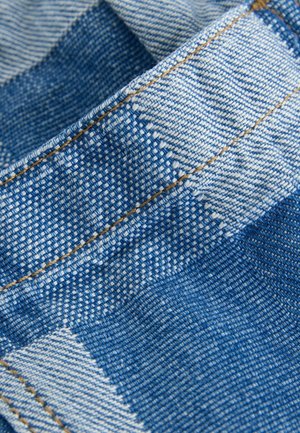 Denimstof med et blåt og hvidt ternet mønster. Karakteristisk beige syning. Teksturen virker vævet med en let glans.