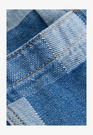 Denimstof met een blauw-wit ruitpatroon. Kenmerkende steken in beige. Textuur lijkt geweven met een lichte glans.