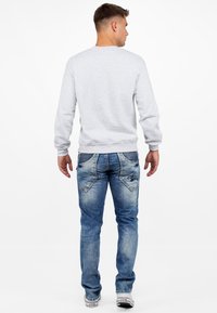 Felpa grigia con maniche lunghe abbinata a jeans azzurri chiari con tasche posteriori decorative e un texture di denim scolorito. Calzature casual visibili.