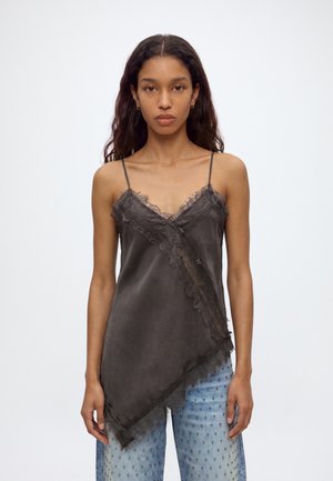 Femme portant un caraco sombre orné de dentelle, un jean à jambes larges imprimé, des talons bleus, et tenant un sac à main blanc.