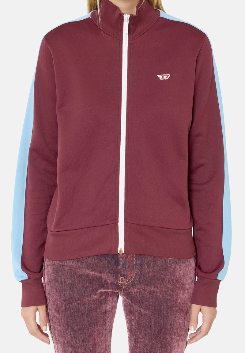 Bordová zipová bunda s vysokým límcem, světlomodrými rukávy a bílým zipem. Na hrudi je malé logo. Měkká textilie.