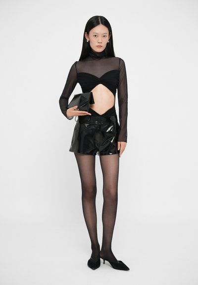 Zwarte doorschijnende langemouwen top met een uitgesneden ontwerp, gecombineerd met hooggetailleerde glanzende zwarte shorts. Een zwarte clutch en doorschijnende panty's maken de look compleet.